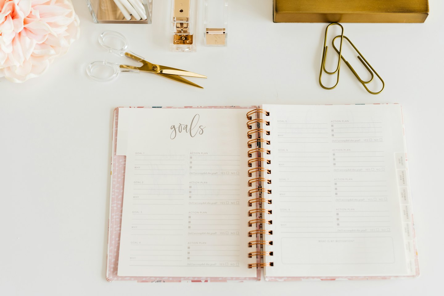 Agenda ouvert avec objectifs et plan d'action sur un bureau blanc avec fournitures.